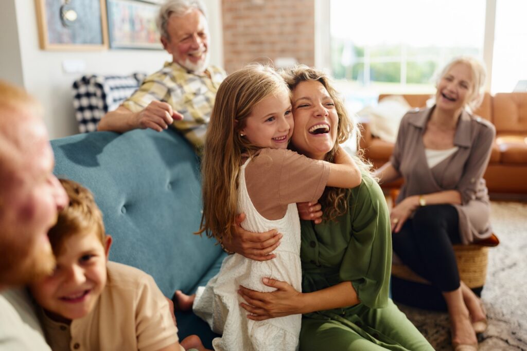 Happy mother and her girl embracing while spending time with their extended family in the living room.